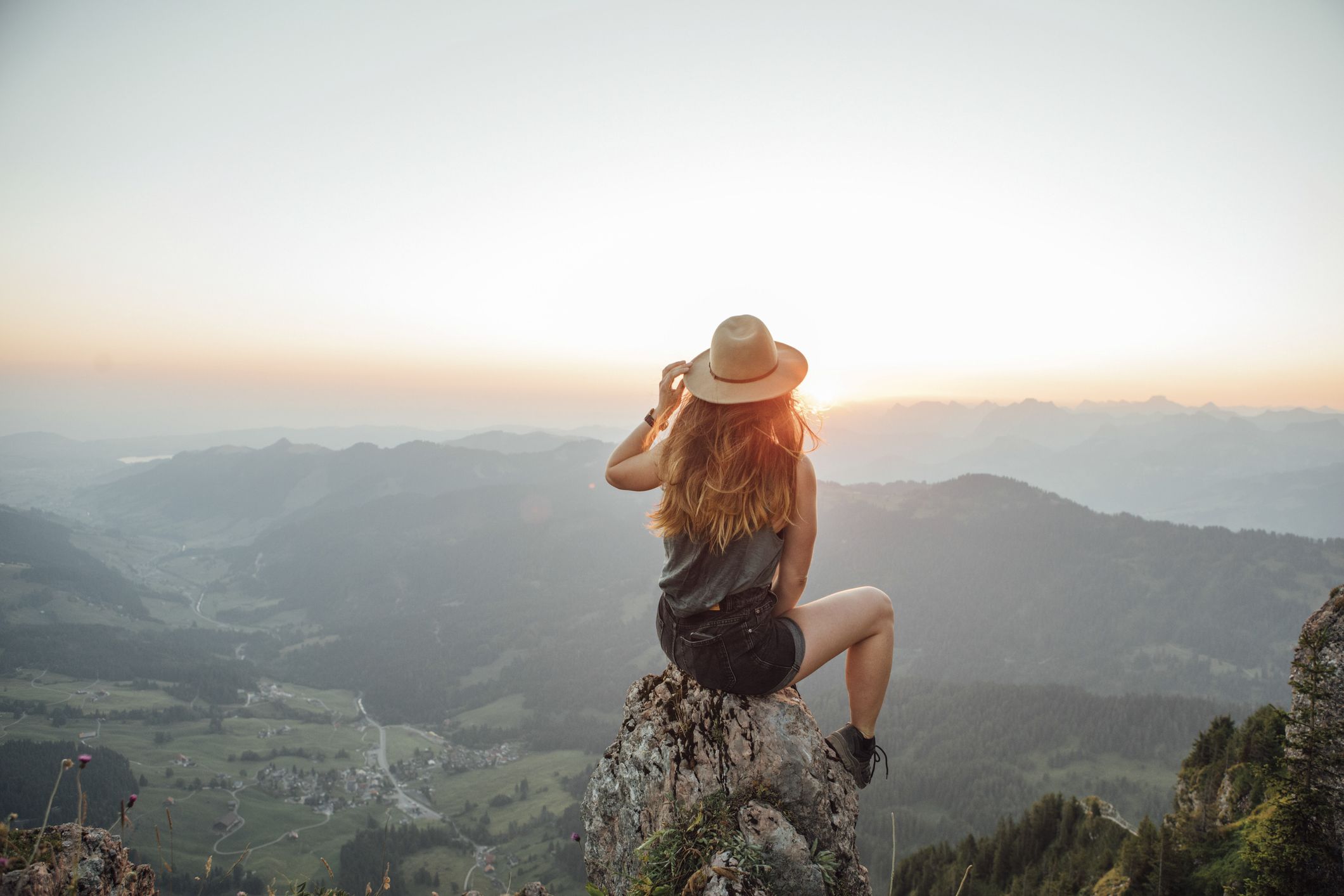 Jonge vrouw die op een rots in de bergen zit en over het landschap uitkijkt.