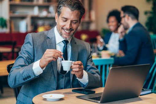Glimlachende man van ongeveer 40 jaar in een café met een laptop en een kop koffie.
