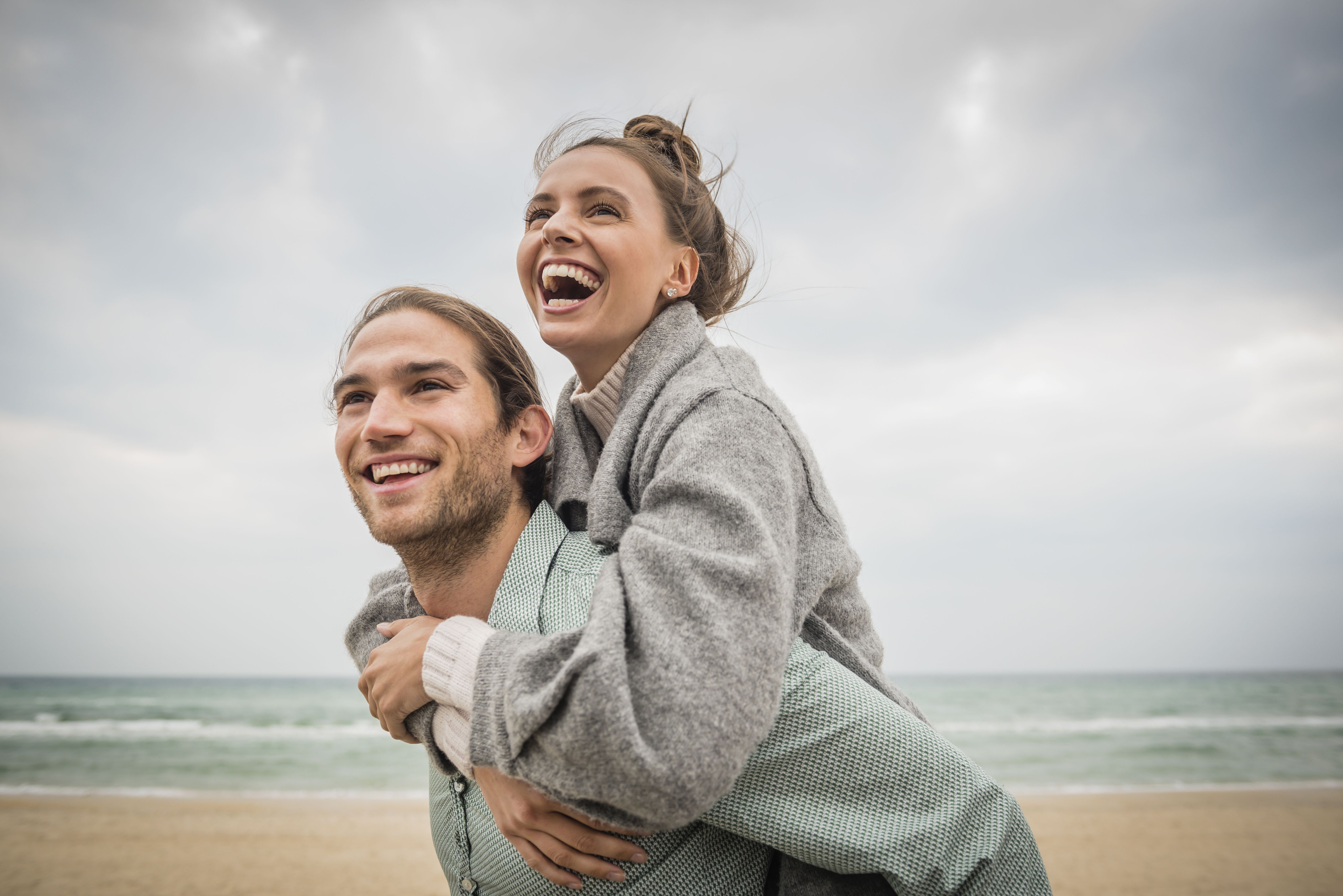 Gelukkig jong koppel op een zonnig strand, waarbij de man de vrouw op zijn rug draagt.