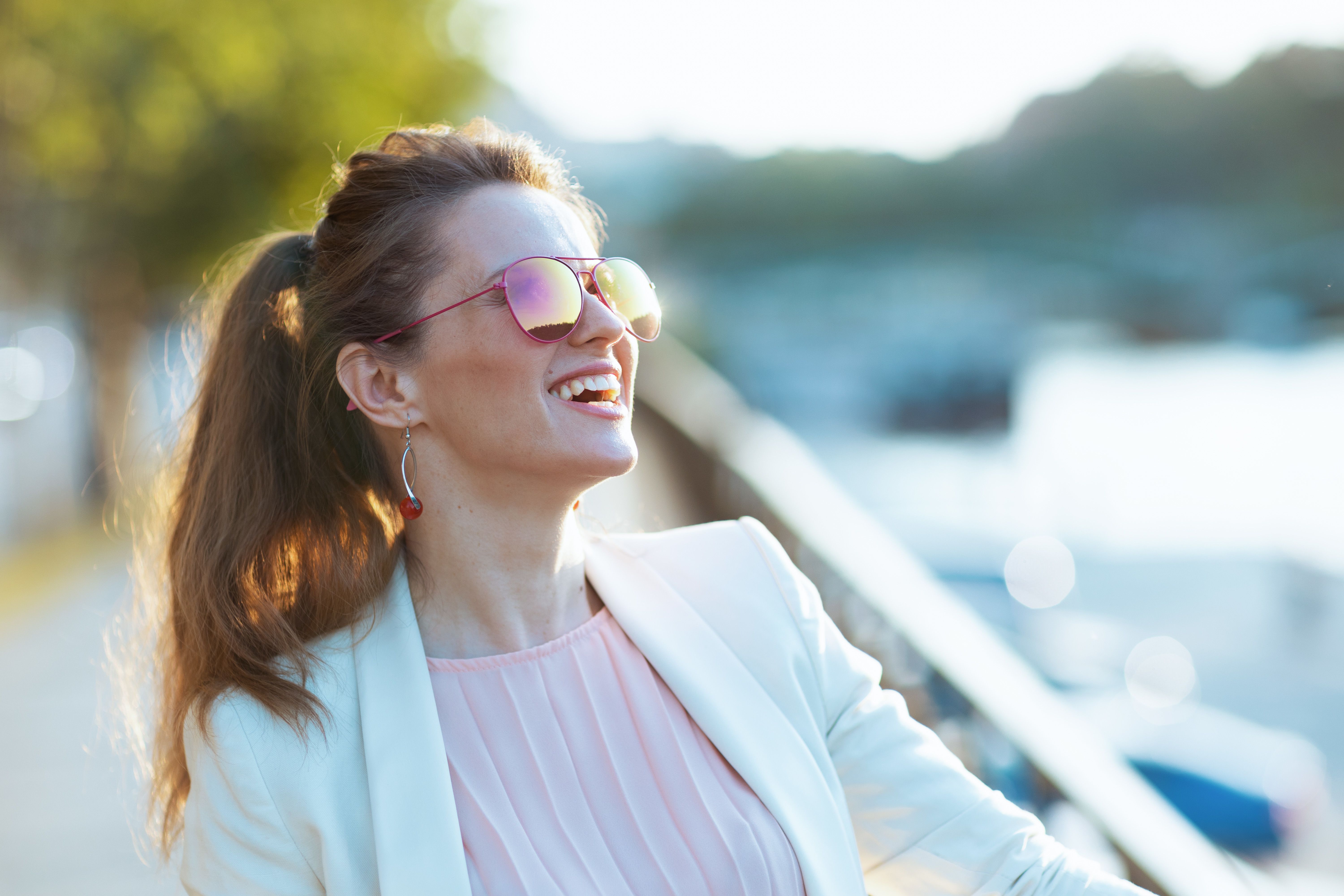 Glimlachende jonge vrouw met zonnebril die op een terras zit.